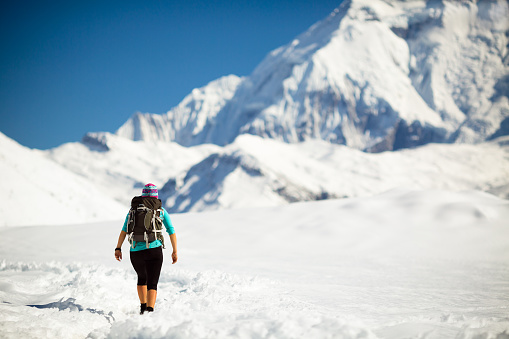Woman hiker walking in beautiful inspirational winter mountains. Trekking and hiking inspiration and motivation in beautiful landscape. Travel and healthy lifestyle outdoors on snow in Himalayas, Nepal.