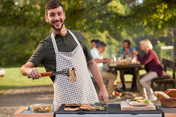 Portrait of man grilling meat at barbecue outdoors Man using serving tongs to grill meat, looking at camera and smiling. serving tongs stock pictures, royalty-free photos & images