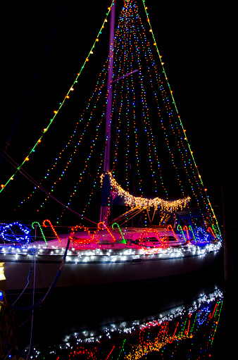 Reflections on the water of a sailboat decked out in Christmas lights give a festive glow to an evening on the water