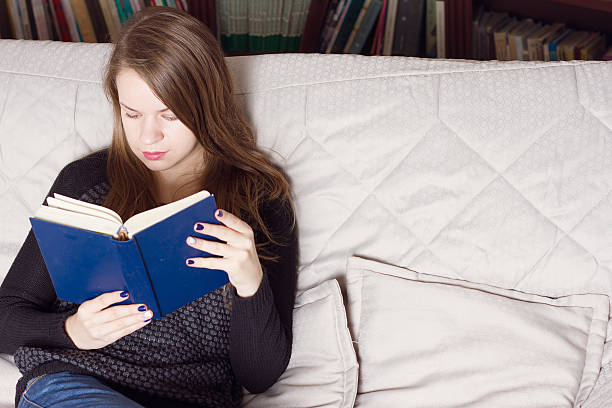 istock young woman reading a book on couch 491774870
