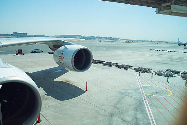 A commercial passenger aircraft is stationed at an airport boarding gate, connected to a jet bridge. Ground staff and baggage carts are visible on the tarmac as preparations for departure continue under a clear blue morning sky.