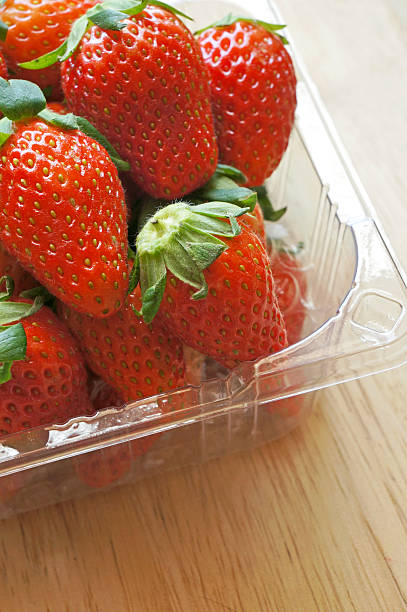 istock Fresh whole strawberries in plastic packing tray on wooden surface 491783331