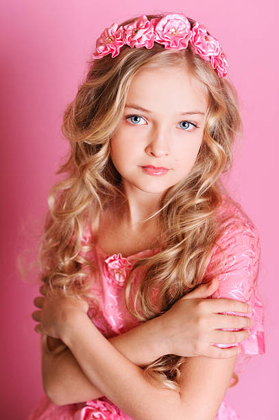 Elegant kid girl posing in studio over pink background. Blonde girl looking at camera.