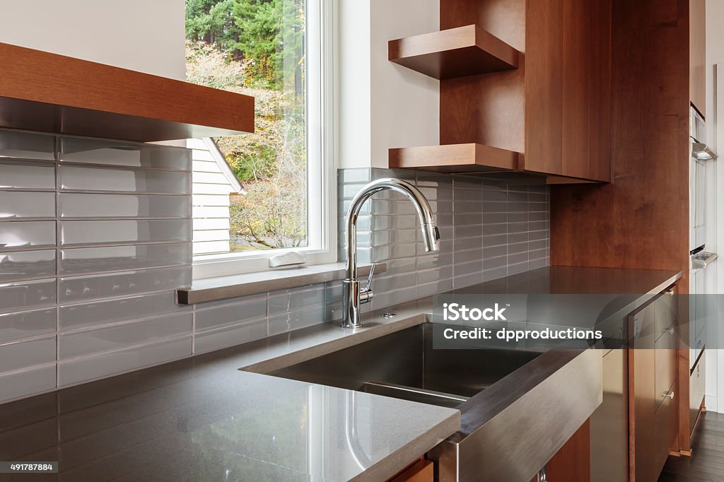 Modern bright sleek kitchen Modern sleek bright kitchen with an undermounted farmhouse type sink with a view, subway tile backsplash, brown cabinets and water faucet Sink Stock Photo