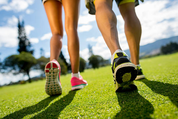 Low angle view of green grass with an unfocused background of a pair of athletes running outdoors with copy space