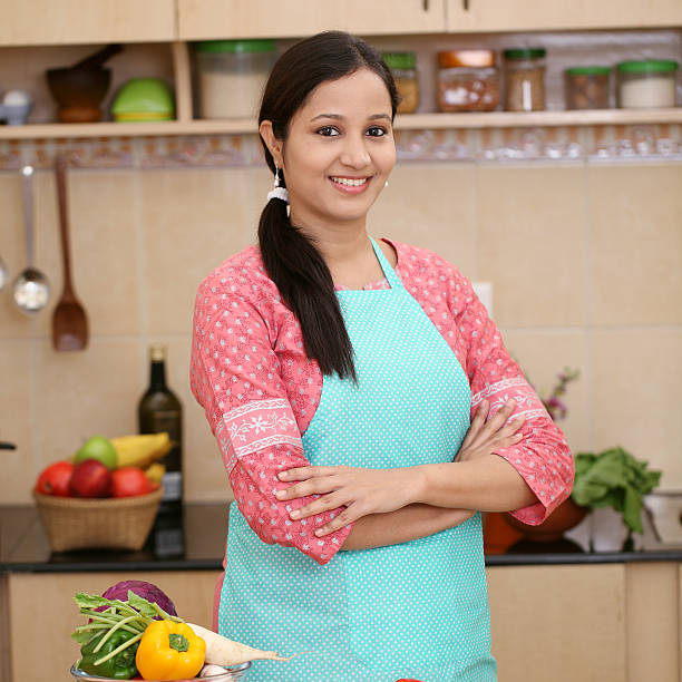 lächelnde junge indische frau mit küche schürze - stereotypical housewife women domestic kitchen brown hair stock-fotos und bilder