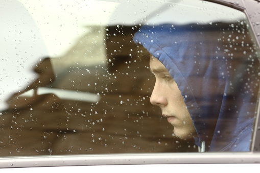 Sad teenager boy worried inside a car looking through the window