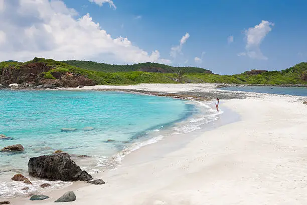 unrecognizable young woman in white swimwear walking along the beach shoreline at West End, St.Thomas, US Virgin Islands