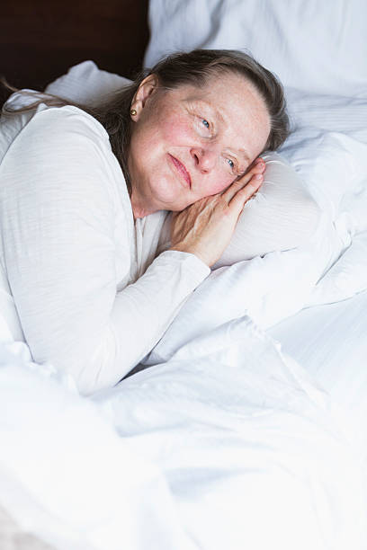 istock Senior woman lying in bed, eyes open, smiling 491807116