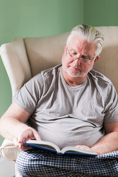 istock Senior man in living room reading book 491810020