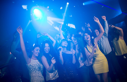 Group of young beautiful people, boys and girls, attending party, dancing, having fun over dark background in neon light. New year celebration. Concept of youth culture, leisure time, fun, lifestyle