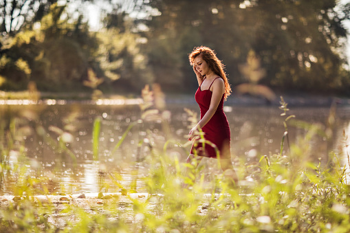 Young redhead woman walking on a beach by the river.