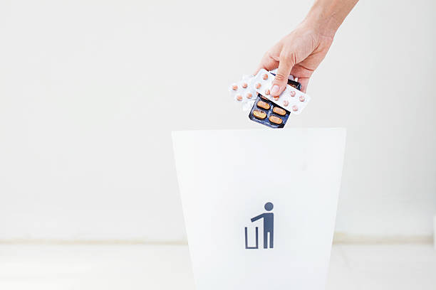hand throwing pills in rubbish bin woman hand holding several package of pills over white bin for rubbish obsolescence stock pictures, royalty-free photos & images