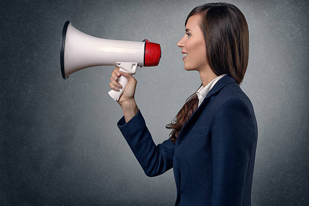 Young Woman Shouting with Megaphone Side View Shot of Young Woman in Long Sleeves Silk Shirt, Shouting with Megaphone on an Abstract Background. conceptional stock pictures, royalty-free photos & images