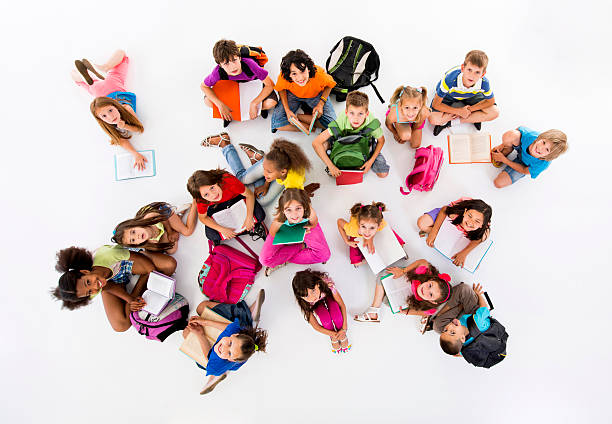 High angle view of school children sitting on the floor and learning while looking at camera. Isolated on white.