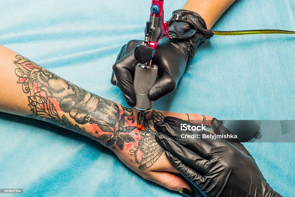 Tattooist demonstrate the process tattoo on hand Close up tattoo artist demonstrates the process of getting black and red tattoo with orange paint. Master works on the professional blue mat in black sterile gloves. Tattoo Stock Photo