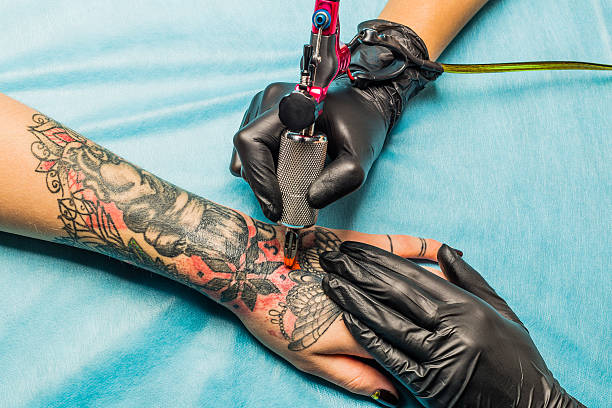 Tattooist demonstrate the process tattoo on hand Close up tattoo artist demonstrates the process of getting black and red tattoo with orange paint. Master works on the professional blue mat in black sterile gloves. tattoo stock pictures, royalty-free photos & images