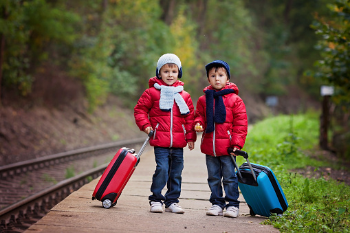 Two boys on a railway station, waiting for the train with suitcases