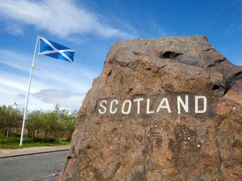 Sign marking the border between England and Scotland, with a Saltire (the national flag of Scotland) flying nearby.