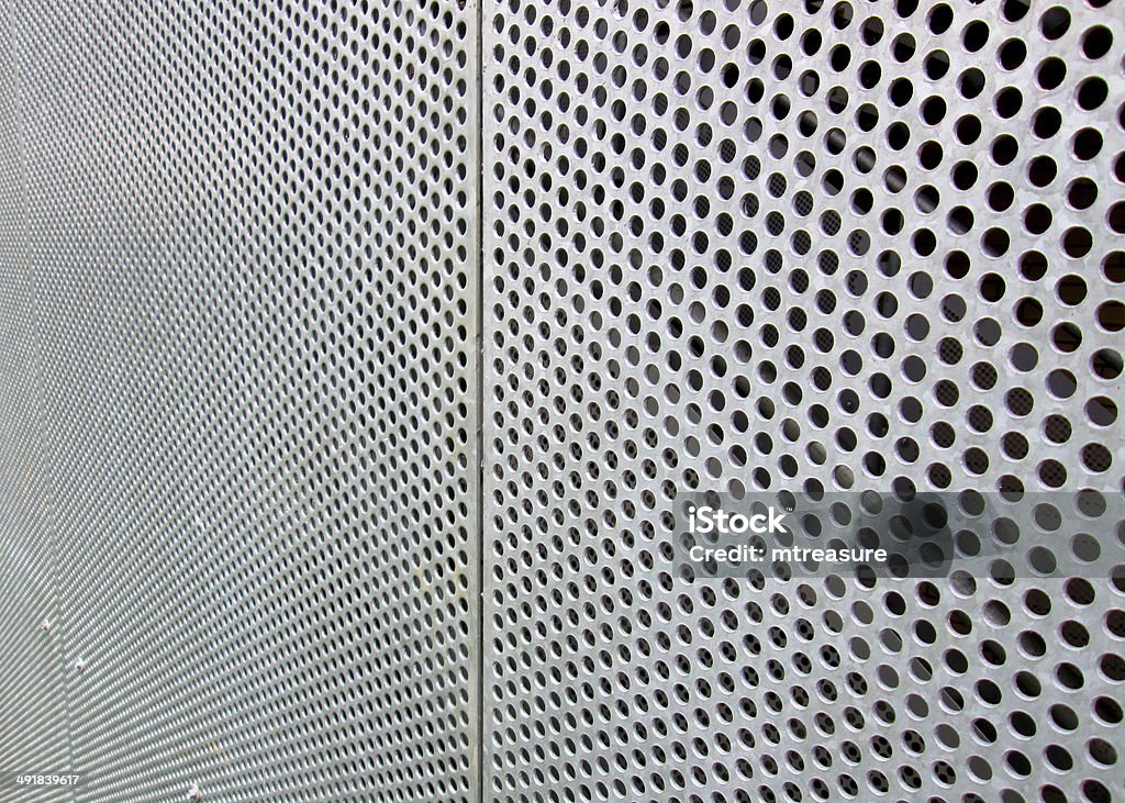 Image of perforated metal sheet with holes forming geometric pattern Photo showing shiny metal perforated sheets of die-cut aluminium, used to clad the side of a building and make it look contemporary.  The geometric pattern is made up of lines of small holes. Perforated Stock Photo