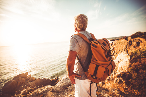 Photo of a senior man, hiking by the sea and exploring the nature, at sunset.