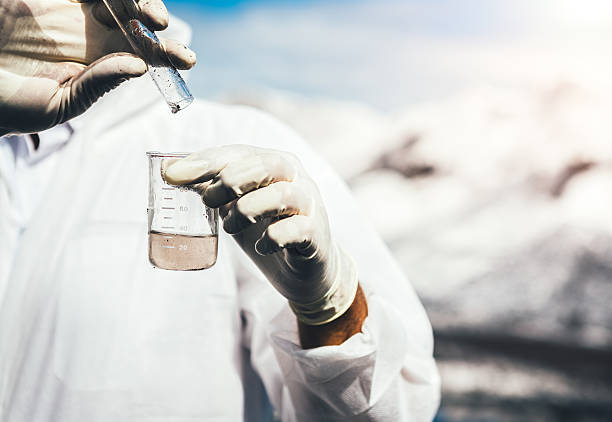 Examing Polluted Water Environmental inspector in white safety suit examing polluted water at industrial site. Heaps of coal covered with white ash in the background. unhygienic stock pictures, royalty-free photos & images