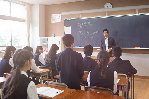 Japanese student stand answering a question to his teacher.