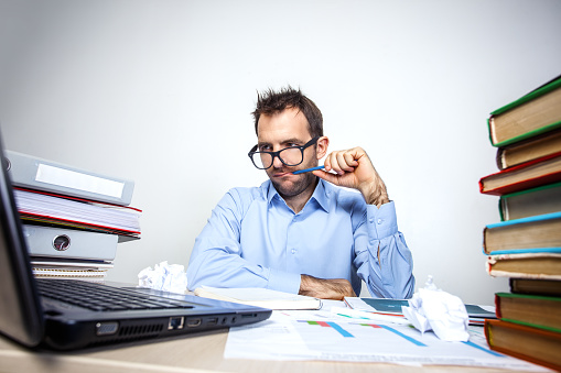 Funny photo of businessman with beard wearing shirt and glasses. Overworked businessman working with laptop at table full of documents. Isolated on white background