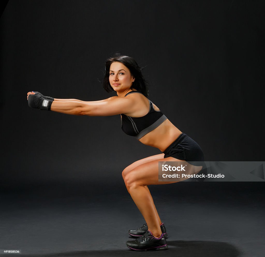 Woman in black fitness suit doing squatting Fitness pose - young sportive woman in gym suit shows squatting in studio at black background 2015 Stock Photo