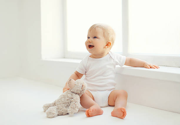 Cute smiling baby with teddy bear toy home in room Cute smiling baby with teddy bear toy sitting at home in white room near window cute baby laughing stock pictures, royalty-free photos & images