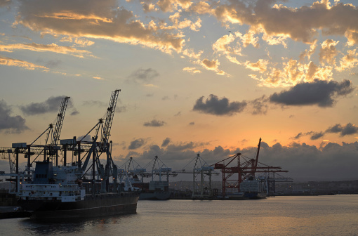 Durban sunset over the container port with gantry cranes pointing to the dying rays of sunshine and haloed clouds