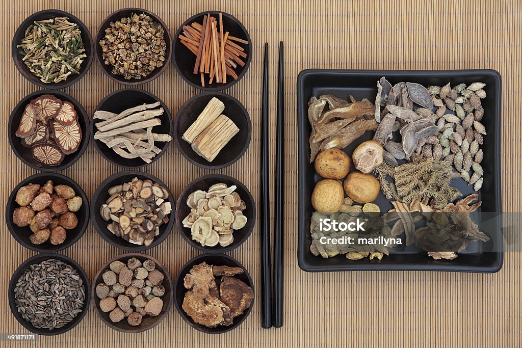 Chinese Herbs Large chinese herbal medicine selection in wooden bowls and square dish with chopsticks over bamboo. Alternative Medicine Stock Photo