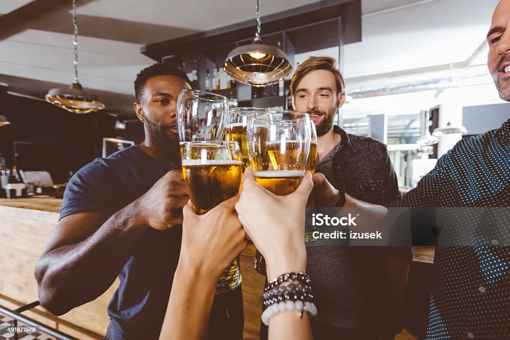 Friends toasting with beer in a pub Multi ethnic group of friends - caucasian and afro american - toasting with beer glasses in the pub. Close up of glasses and hands. Beer Glass Stock Photo
