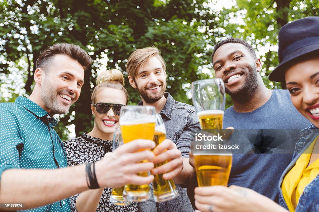 Multi ethinc friends drinking with beer outdoors Multi ethnic group of happy friends - caucasian and afro american - toasting with beer glasses outdoor, in the park.  Beer Glass Stock Photo