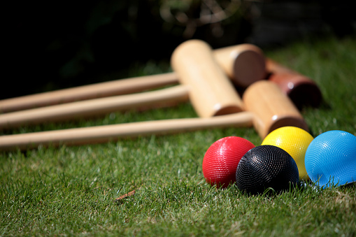 Croquet mallet and colourful balls lying on a lawn of green grass in the sunshine. Useful for children or at events such as weddings