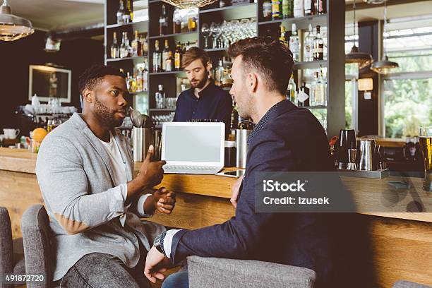 Afro American Man Talking With Colleague In Pub Using Laptop Stock Photo - Download Image Now