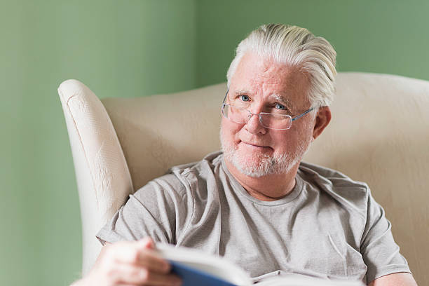 istock Senior man in living room reading book 491873402