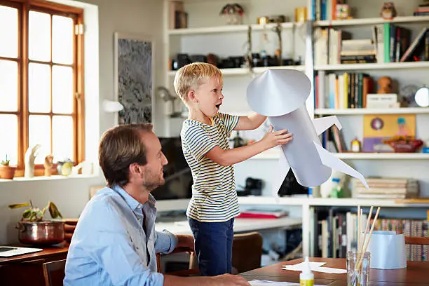 Father and son building rocket at table in living room