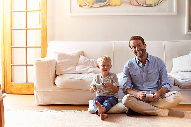 Father and son playing video games Father and son playing video games together at home kid sitting cross legged stock pictures, royalty-free photos & images