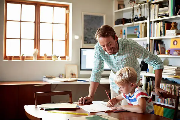 Father helping son with homework at table in living room