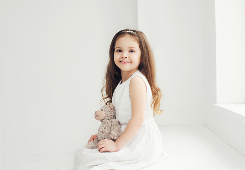 Beautiful little girl with teddy bear in white room