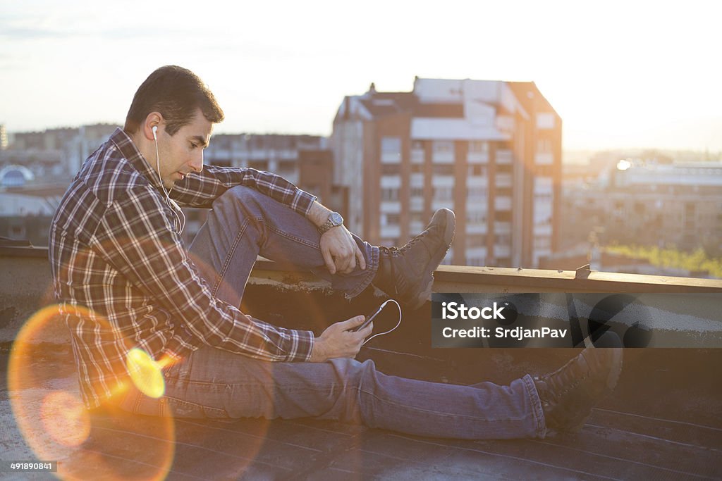 Young man listen music in sunset Young man listen to the music on smartphone on the top of building with city in beckground Adult Stock Photo