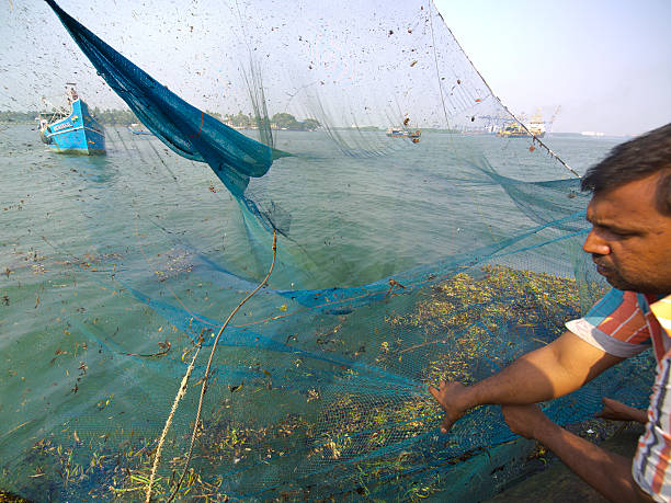 Empty Fishing Net Cochin, India - December 20, 2013: Fisherman is looking at is empty fishing net on Cochin shore. In background is fisherman’s boat with island on horizon. cochin kerala india chinese fishing net stock pictures, royalty-free photos & images