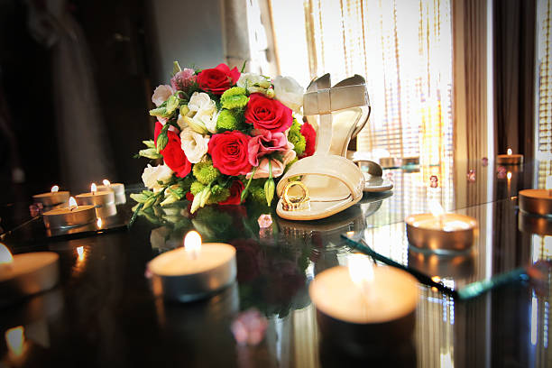 Wedding bouquet, rings, and  Wedding Women's Shoes are on the table. The table is full with little candles.