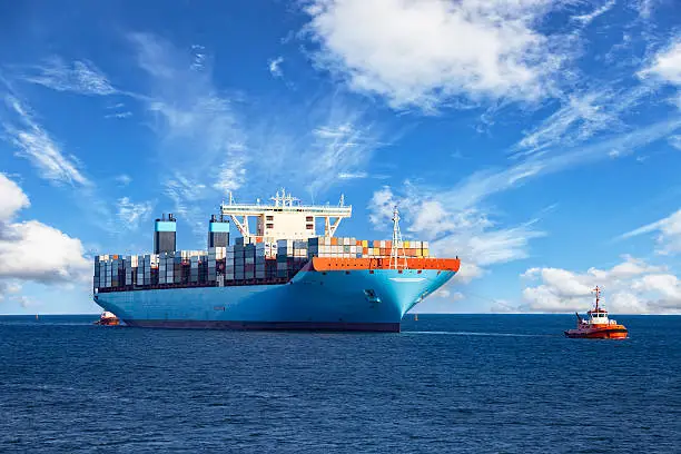 Tugboats assisting container cargo ship to harbor.