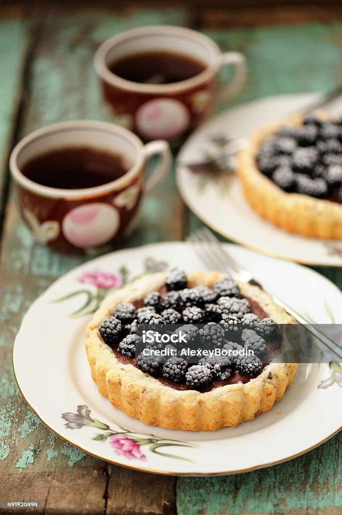 Fancy cake with blackberries and chocolate cream with icing Fancy cake with blackberries and chocolate cream with icing sugar with two cups of black tea vertical 2015 Stock Photo