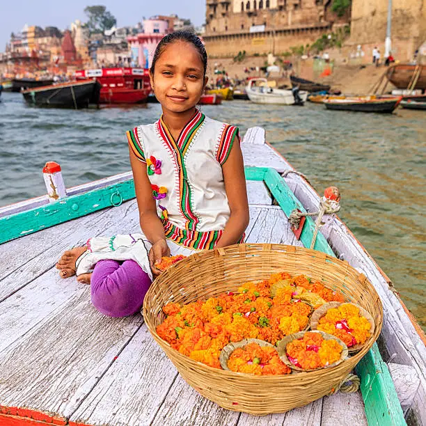 Little girl selling flower candles - a small candles inside a cup made from leaves and flowers. The Ganga is the most sacred river to Hindus.It is worshipped as the goddess Ganga in Hinduism.