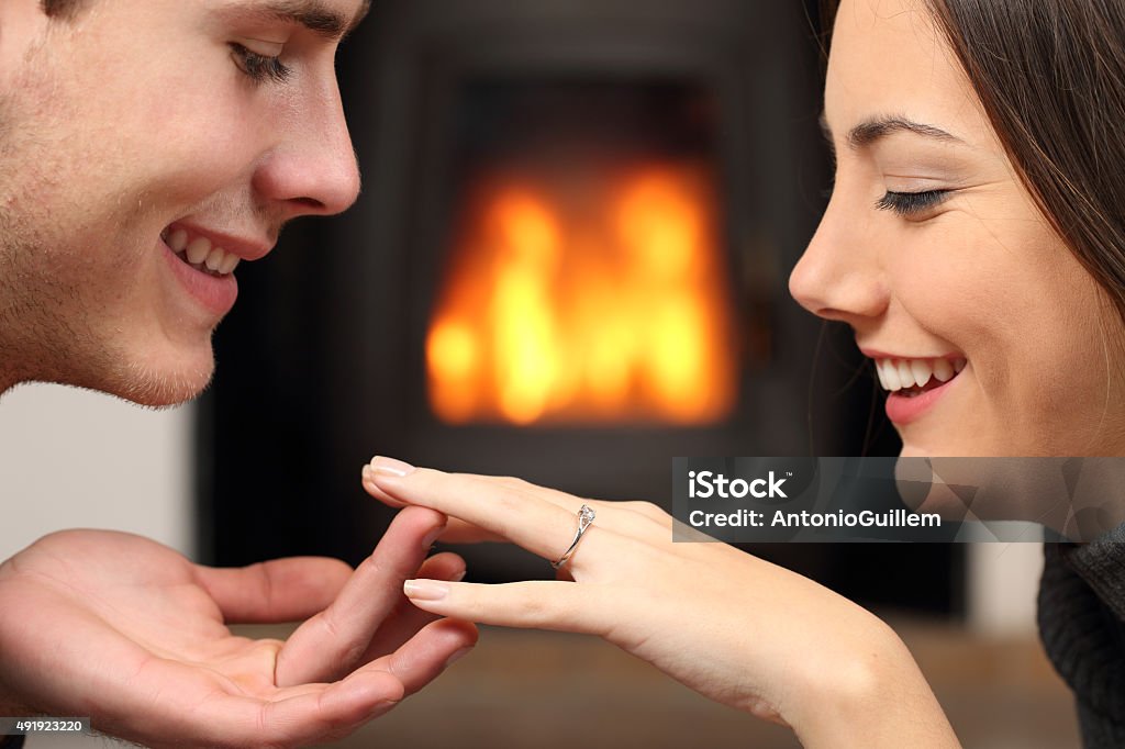 Couple looking a engagement ring after proposal Couple looking a engagement ring after proposal at home with a fire place in the background 2015 Stock Photo