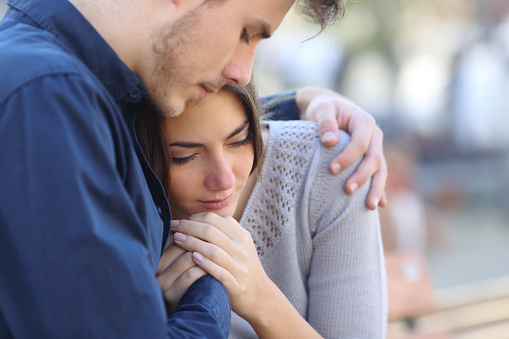 Man comforting his sad mourning friend embracing her in a park