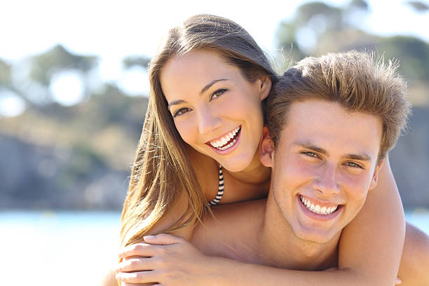 Couple with perfect smile posing on the beach Happy couple with perfect smile and white teeth posing on the beach looking at camera heterosexual couple stock pictures, royalty-free photos & images